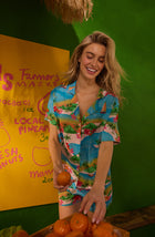 A Lady Wearing Amelia Short Woven Pj Set In Sunset Escape shown in a front view pose holding oranges