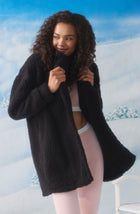 A Lady Wearing Blake Sherpa Short Jacket In Black standing elegantly in a beautiful winter background setup, surrounded by snow