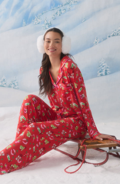 A Lady Wearing Collette Knit Pj Set In Country Claus sitting elegantly on a winter skating board in a snowy winter landscape while wearing stylish snow headphones