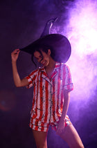 A Lady Wearing Siennna Short Knit Pj Set In Haunted Happy Hour in a standing pose against a purple flash light
