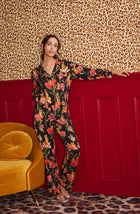 A Lady Wearing Stella Knit Pj Set In Flora & Fierce standing in a front facing view against a leopard print wall and positioned next to a yellow sofa