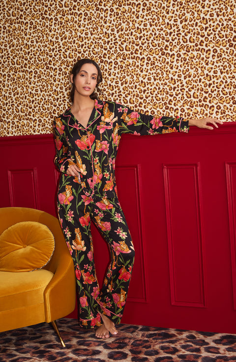 A Lady Wearing Stella Knit Pj Set In Flora & Fierce standing in a front facing view against a leopard print wall and positioned next to a yellow sofa