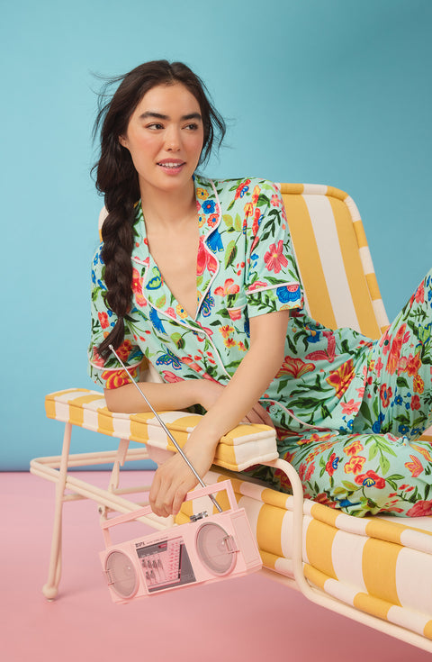 A Lady Wearing Dakota Long Knit Pj Set In Aqua Fleur shown in a laying pose holding a pink radio