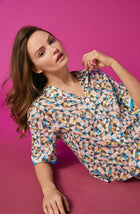 A lady wearing a multi colour short sleeve top with a tile pattern.