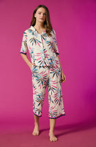 A lady wearing a white short sleeve pajama set with multi colour palm leaves pattern
