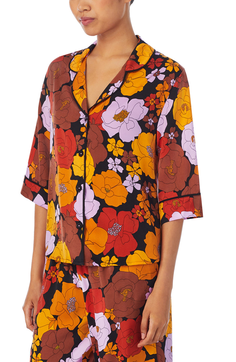 A lady wearing a black elbow sleeve gramercy top with multi color floral pattern.