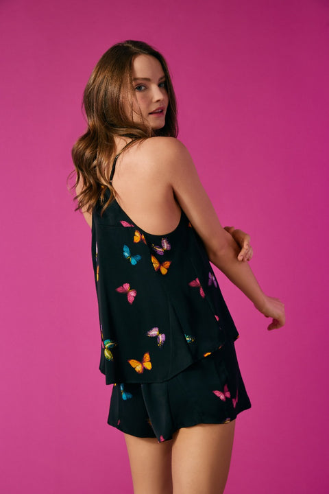 A girl wearing a black sleeveless pajama set with multi colour butterflies.