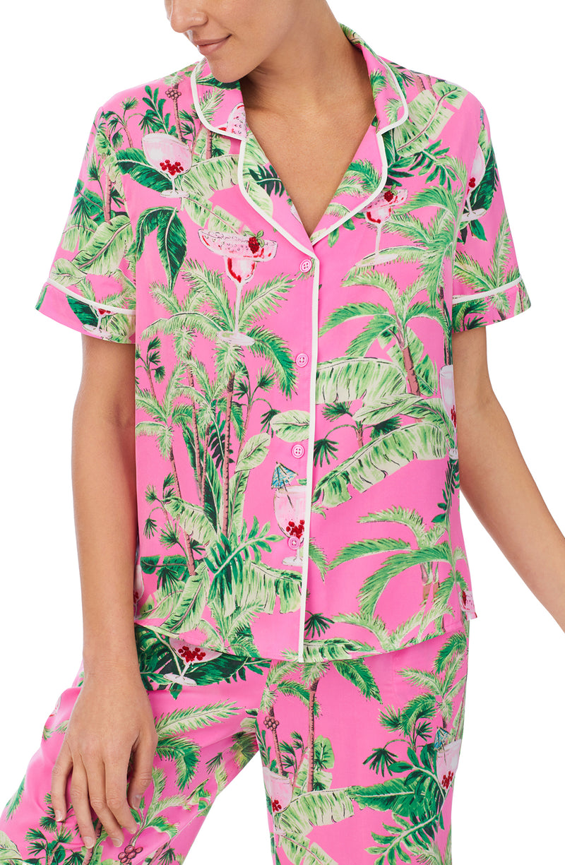 A lady wearing a pink short sleeve top with green floral pattern.