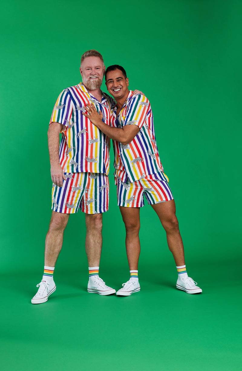 Two men wearing a pride short sleeve pj set with prowling pattern.
