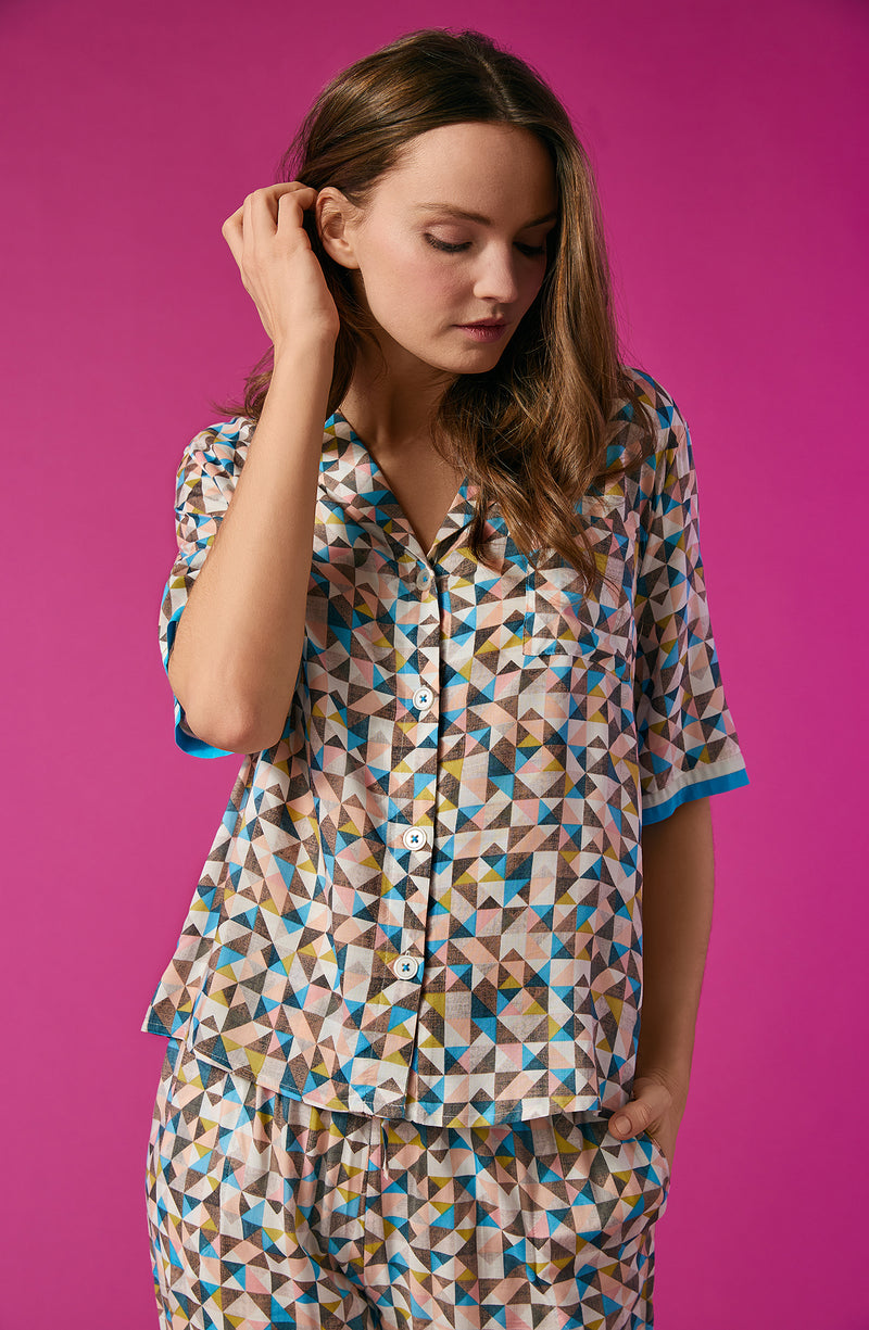 A lady wearing a multi colour short sleeve top with a tile pattern.
