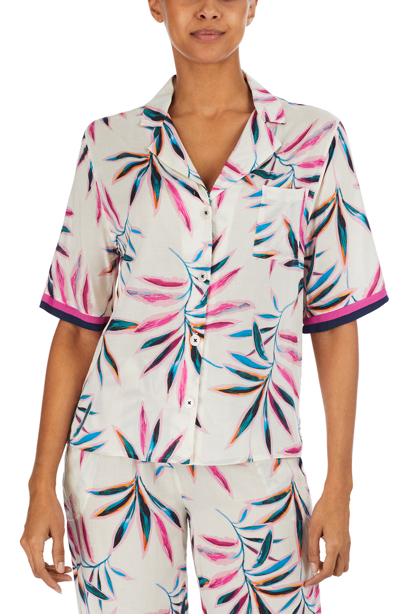 A lady wearing a white short sleeve top with multi colour palm leaves pattern