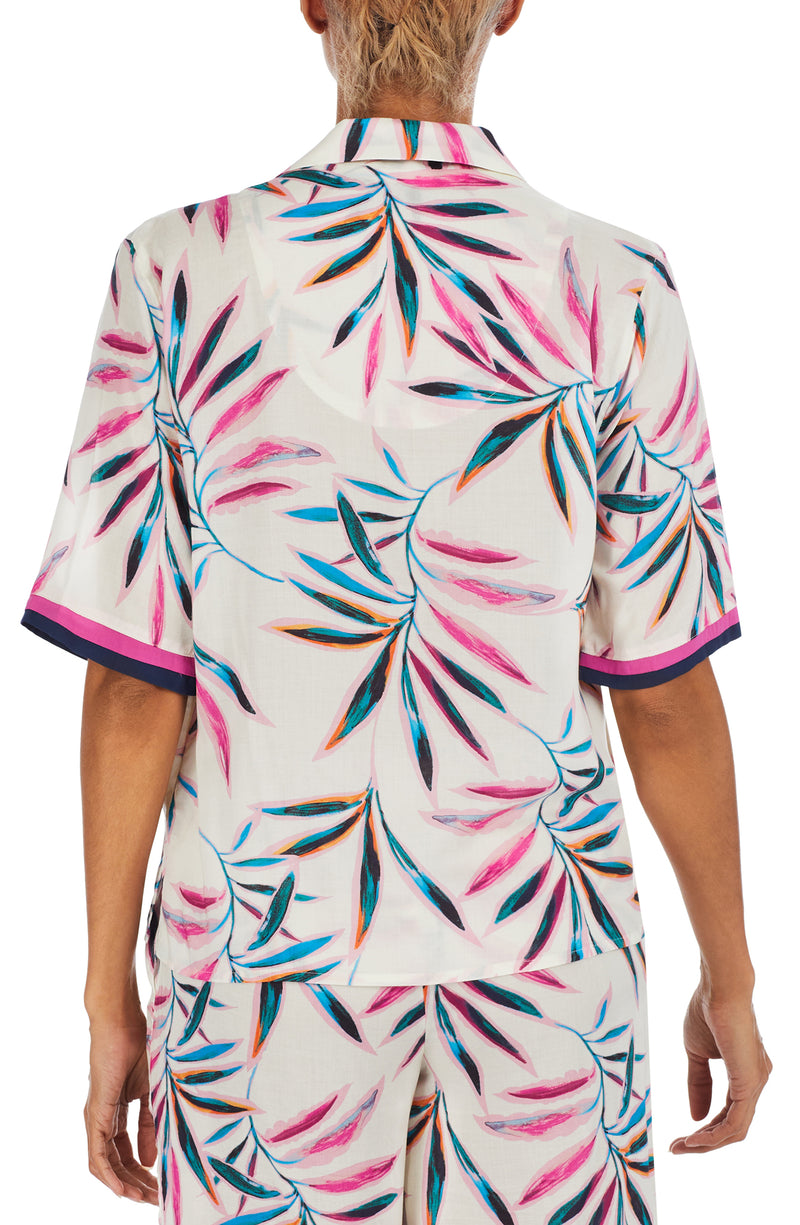 A lady wearing a white short sleeve top with multi colour palm leaves pattern