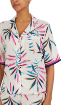 A lady wearing a white short sleeve top with multi colour palm leaves pattern
