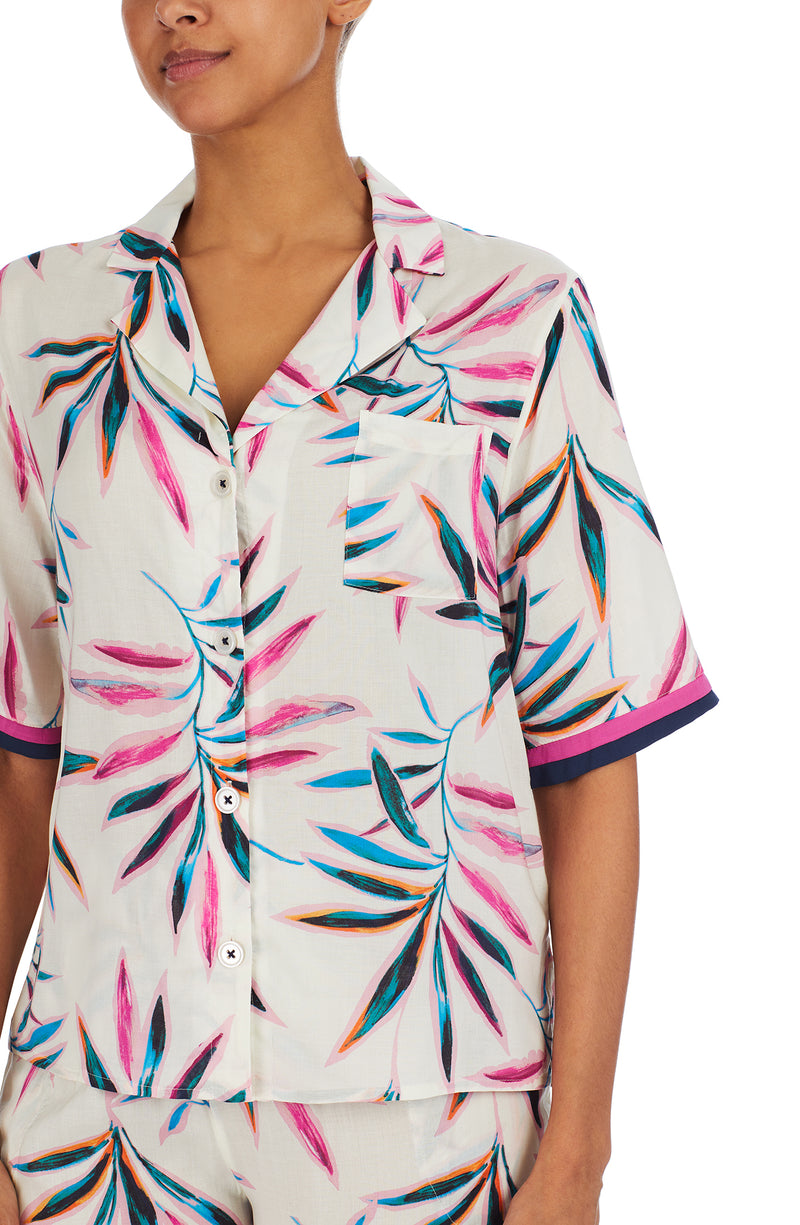 A lady wearing a white short sleeve top with multi colour palm leaves pattern