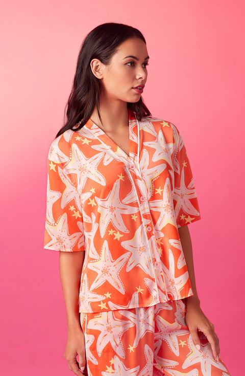 A lady wearing orange short sleeve tilden pj set with star struck print.