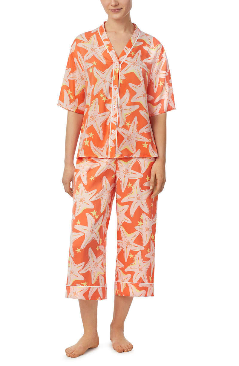 A lady wearing orange short sleeve tilden pj set with star struck print.