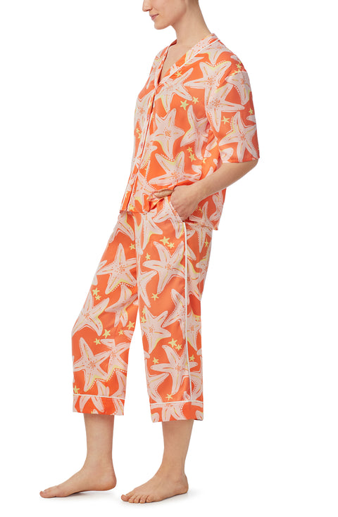 A lady wearing orange short sleeve tilden pj set with star struck print.