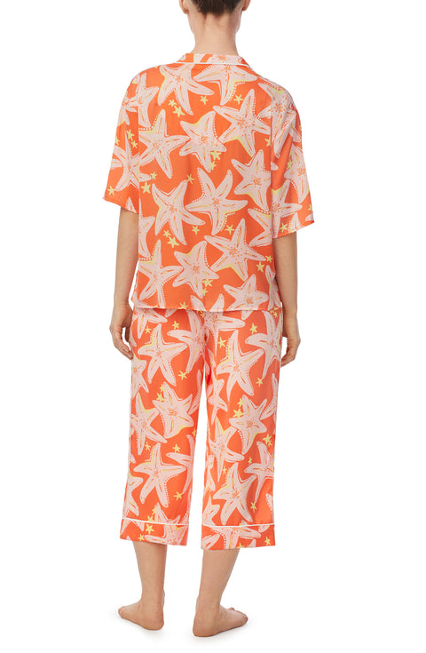 A lady wearing orange short sleeve tilden pj set with star struck print.