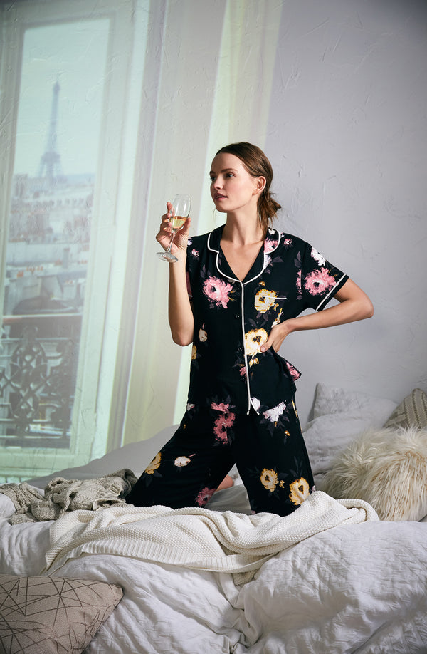 A girl wearing a black short sleeve top and crop pant pajama set with floral design.