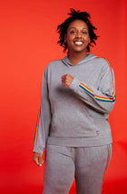 A lady wearing a grey long sleeve unisex reese hoodie with pride stripes in side.