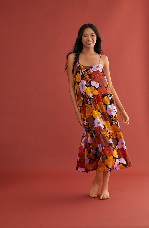 A lady wearing a black sleeveless maxi slip with multi color floral pattern.