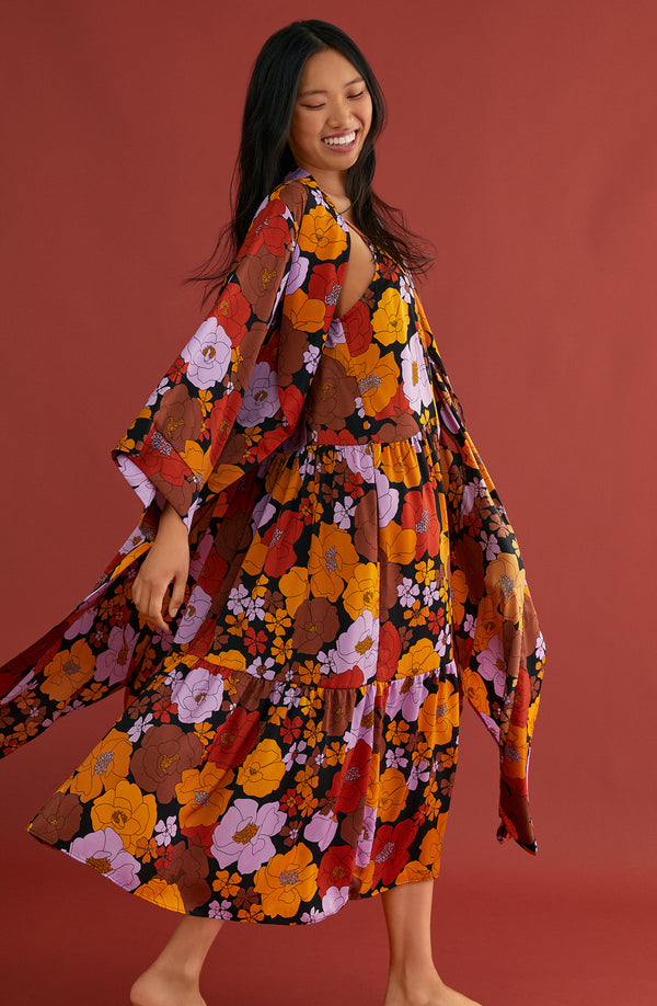 A lady wearing a black long sleeve maxi robe with multi color floral pattern.